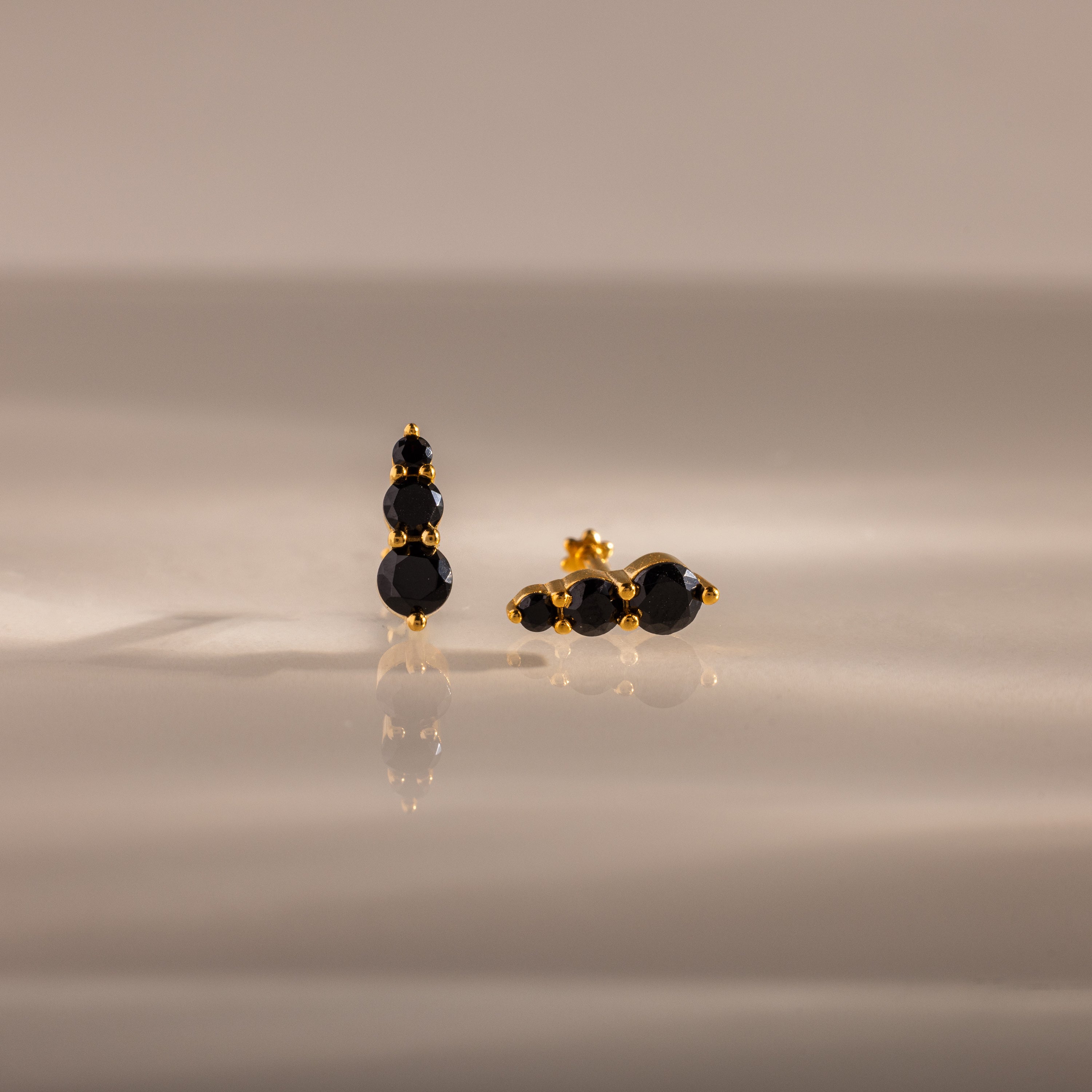Ombre Onyx Flatback Studs featuring three round black stones on a gold setting, displayed on a smooth, reflective surface—a perfect personalized gift.