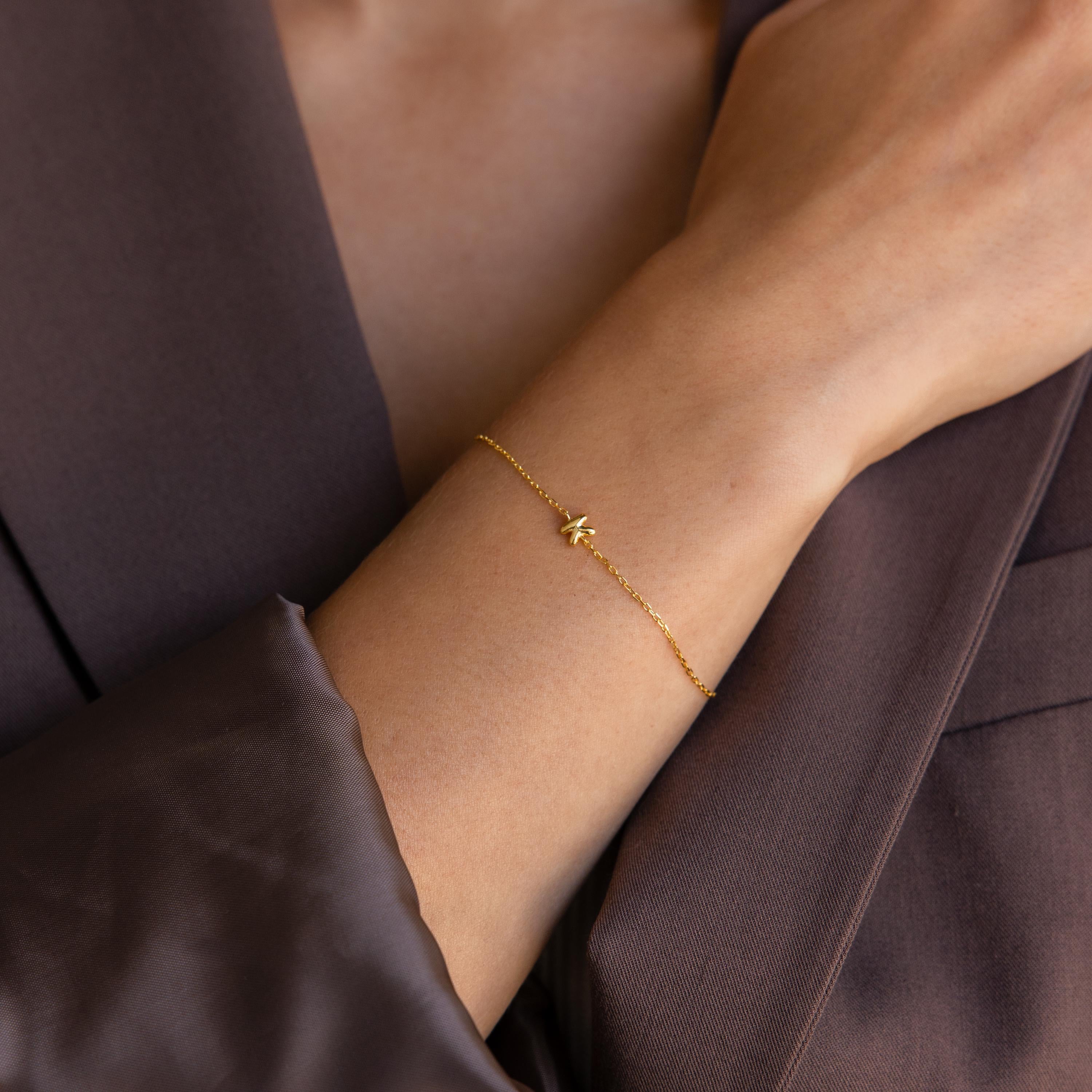 Model wearing a dainty bubble initial charm bracelet with the letter K.