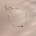 Close up of a dainty silver bubble letter M bracelet against a neutral background.