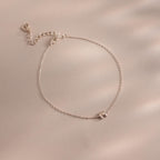 Close up of a dainty silver bubble letter M bracelet against a neutral background.