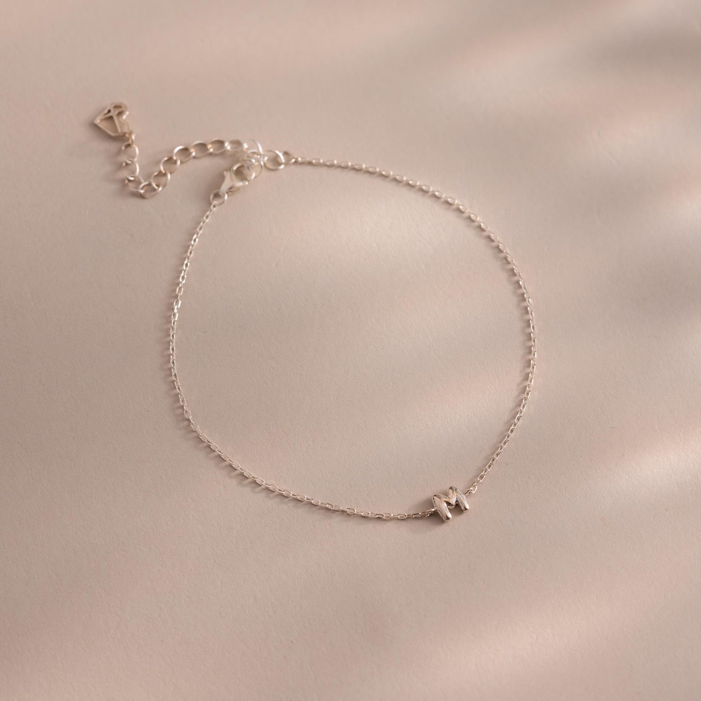 The Bubble Initial Bracelet is a delicate silver personalized piece featuring an initial charm, ideal for everyday wear and beautifully displayed on a light beige surface.