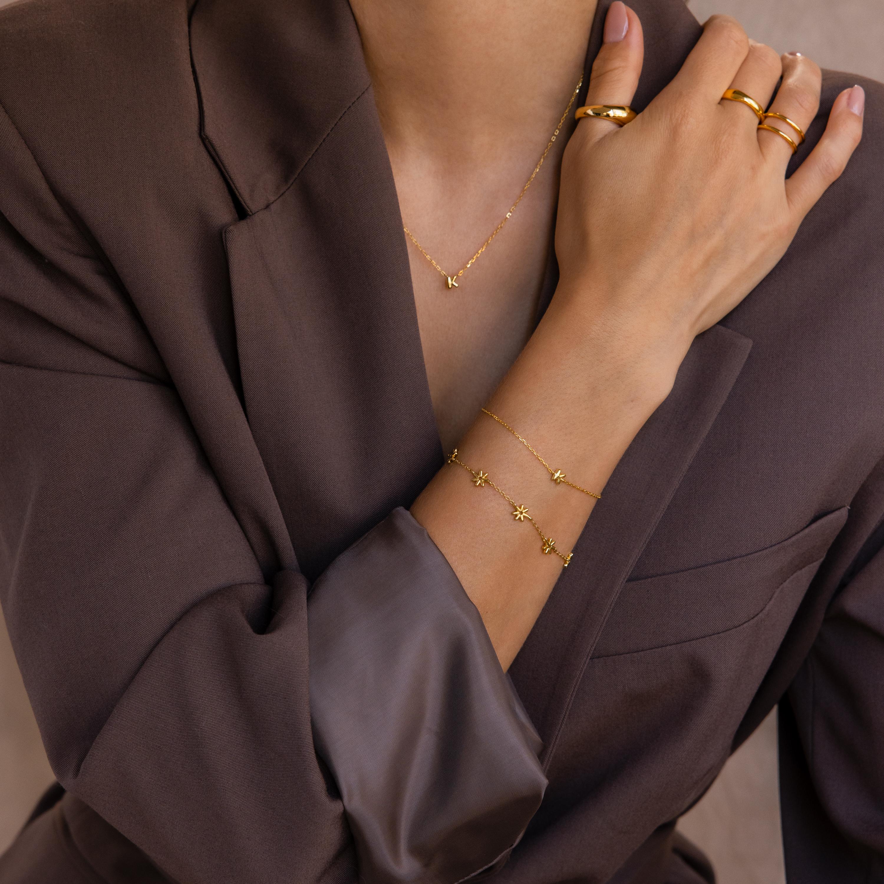 Model wears gold bubble initial bracelet with the letter K. She pairs it with a matching bubble necklace and other gold jewelry.