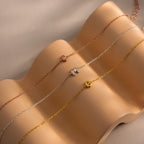 Three Bubble Initial Bracelets in rose gold, silver, and gold—with the letters E, M, and B—rest on a soft wave-shaped display.