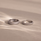Two Pave Stacking Rings in silver, adorned with diamond-studded details, rest on a soft beige surface as gentle light and shadows accentuate their sparkling bands.