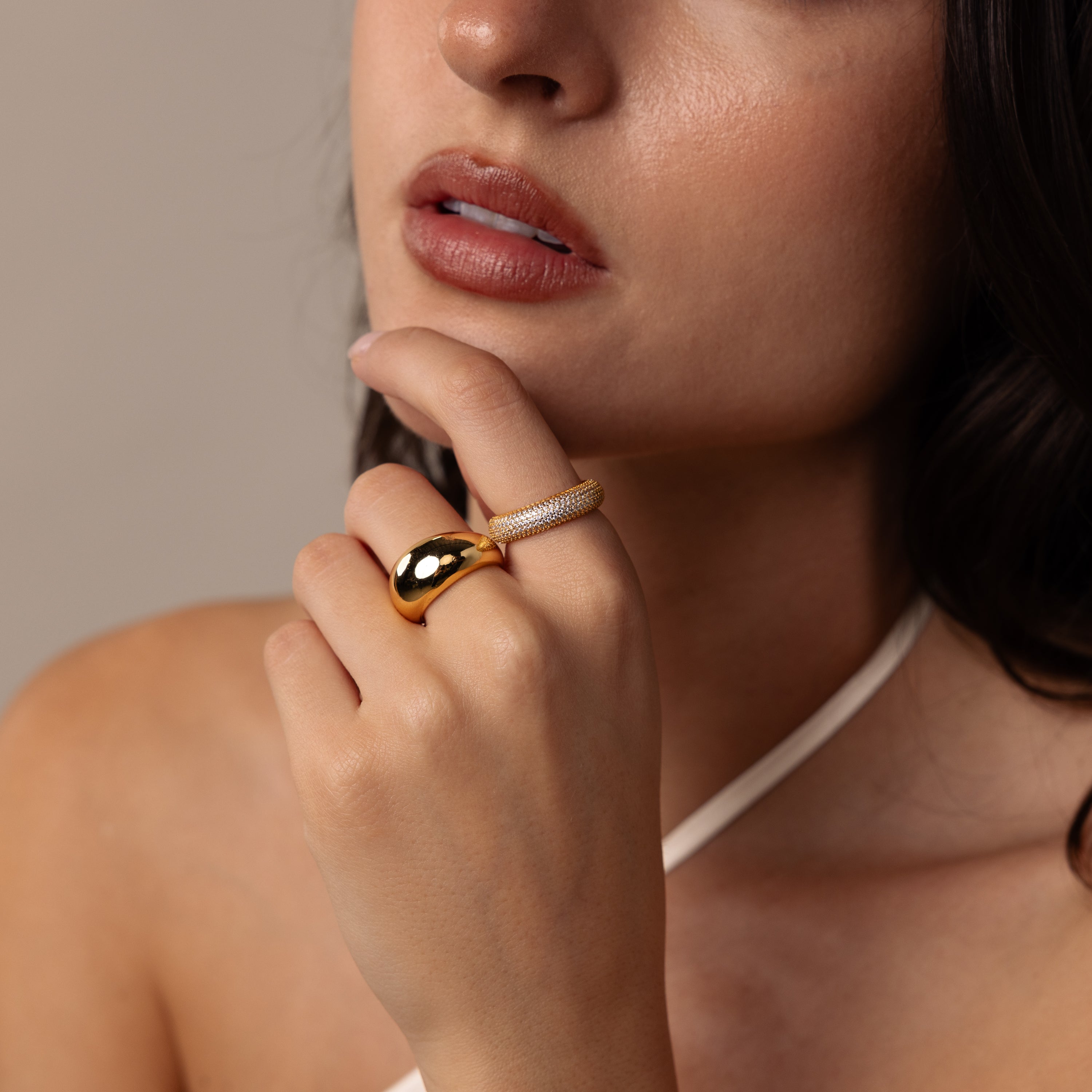A woman touches her lips, wearing the Bold Pave Stacking Ring and a white halter top, with soft lighting on her face.