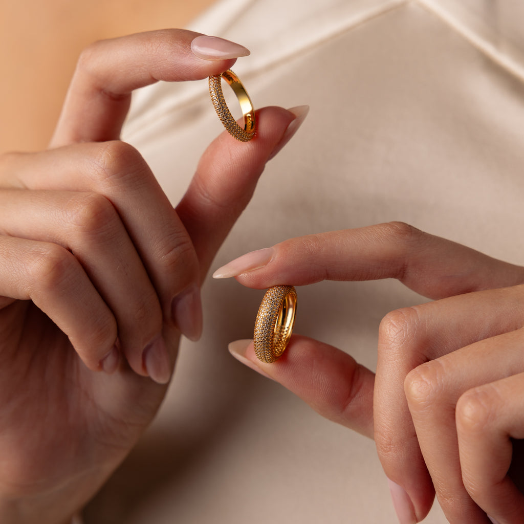 Close-up of hands holding two Pave Stacking Rings—a classic wedding band and a dome band—against a cream-colored fabric background.