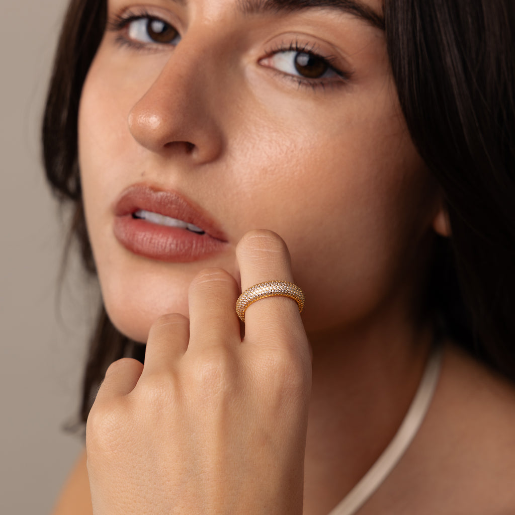 A woman with brown hair wears Pave Stacking Rings, holding her hand near her face and looking at the camera.