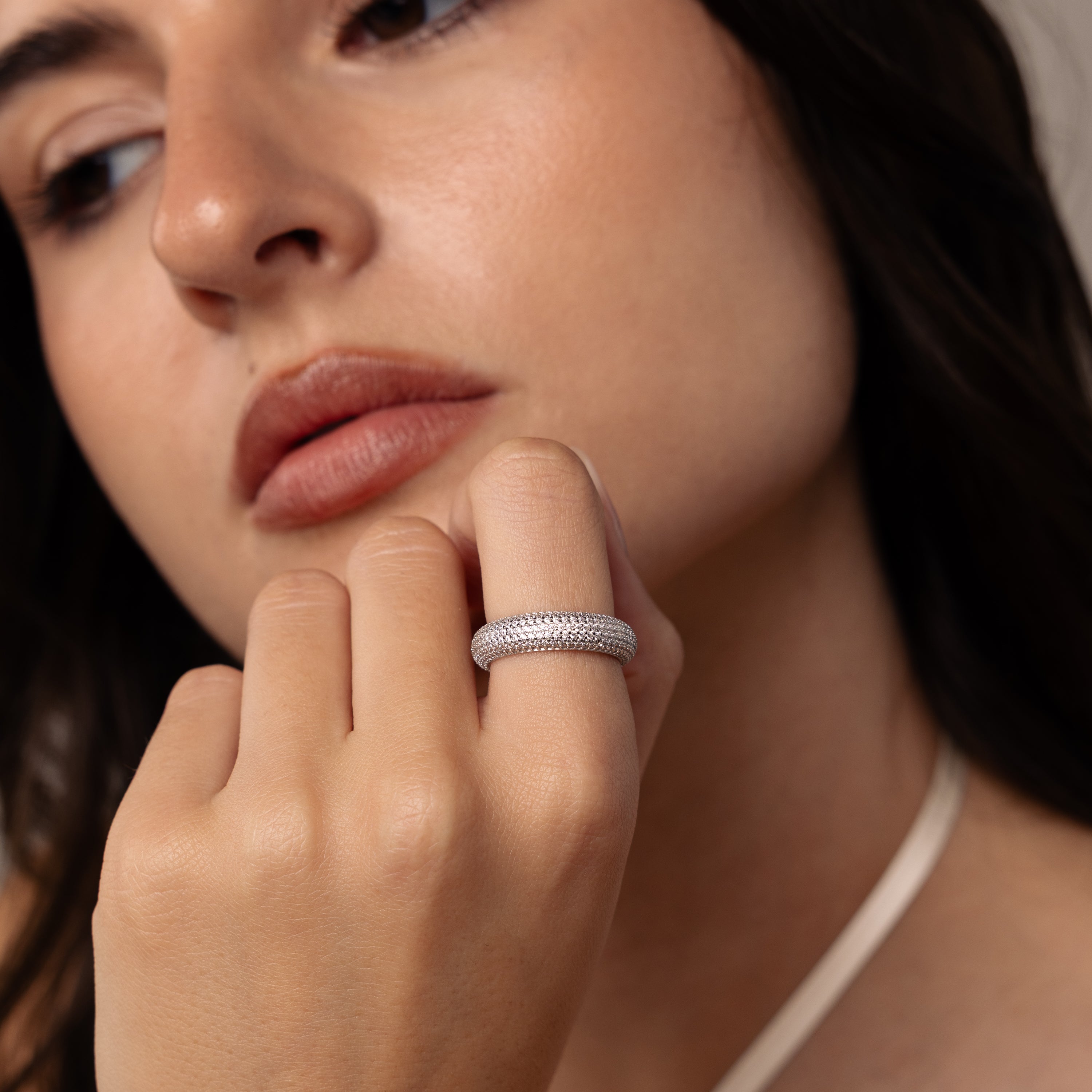 A woman with soft makeup rests her chin on her hand, highlighting the sparkling Pave Stacking Ring on her finger.