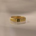 Ribbed Peridot Band with a square cut stone is reflected on a smooth, light-colored surface.