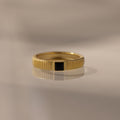 The Ribbed Onyx Band is a gold birthstone ring featuring a black square-cut onyx set in the center, beautifully displayed on a smooth, reflective surface.