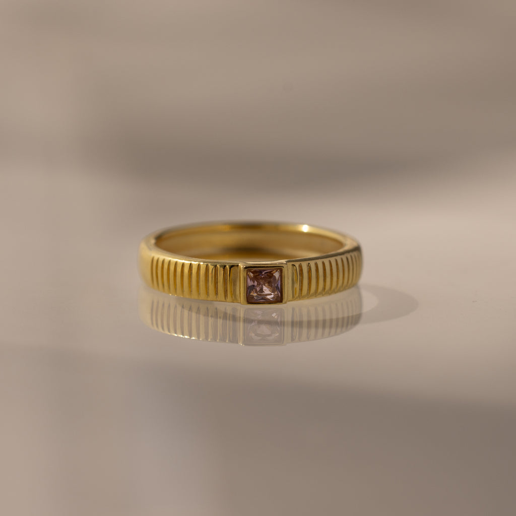 The Ribbed Pink Tourmaline Band is a gold stacking ring with a textured pink tourmaline band and a small square gemstone, making it an elegant choice for a birthstone ring.