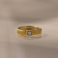 The Ribbed Diamond Band features gold ribbing and a square-cut center diamond, perfect for stacking or wearing alone. Shown on a neutral background.