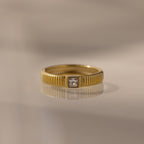 The Ribbed Diamond Band features gold ribbing and a square-cut center diamond, perfect for stacking or wearing alone. Shown on a neutral background.