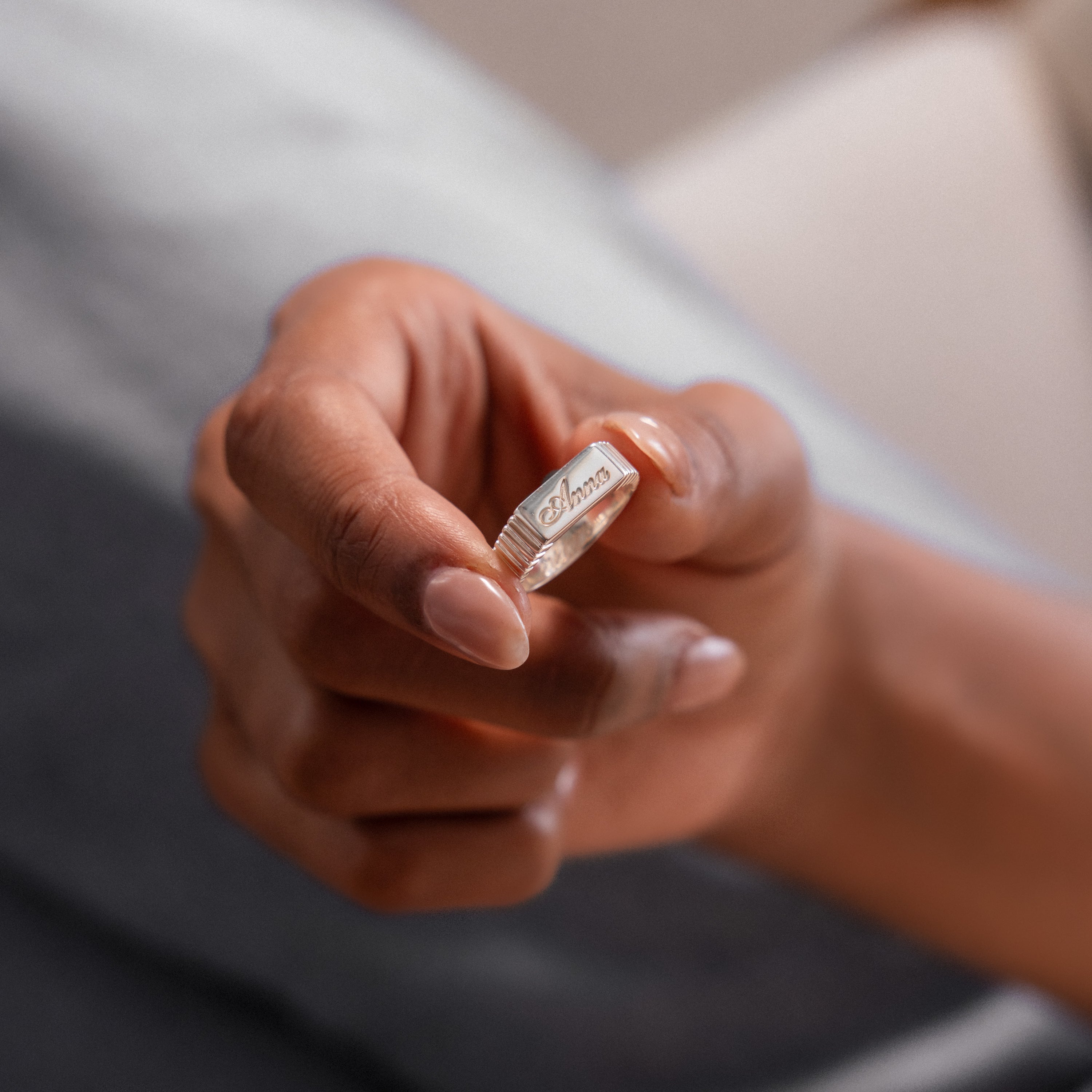 A hand displays the Ribbed Name Signet Ring in Silver, engraved with the name Anna, against a blurred background.