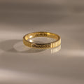 The Ribbed Name Ring in 18K Gold, engraved with "Charlotte" and the date 08.14.96, rests on a smooth, reflective surface—an elegant example of personalized jewelry.