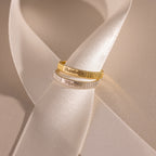 The Ribbed Name Ring, available in gold or silver, shines on a white satin ribbon under soft light—ideal as a personalized gift or custom engraved keepsake.