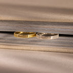 A gold Ribbed Name Ring and a silver engraved ring rest side by side on the edge of a closed beige book.