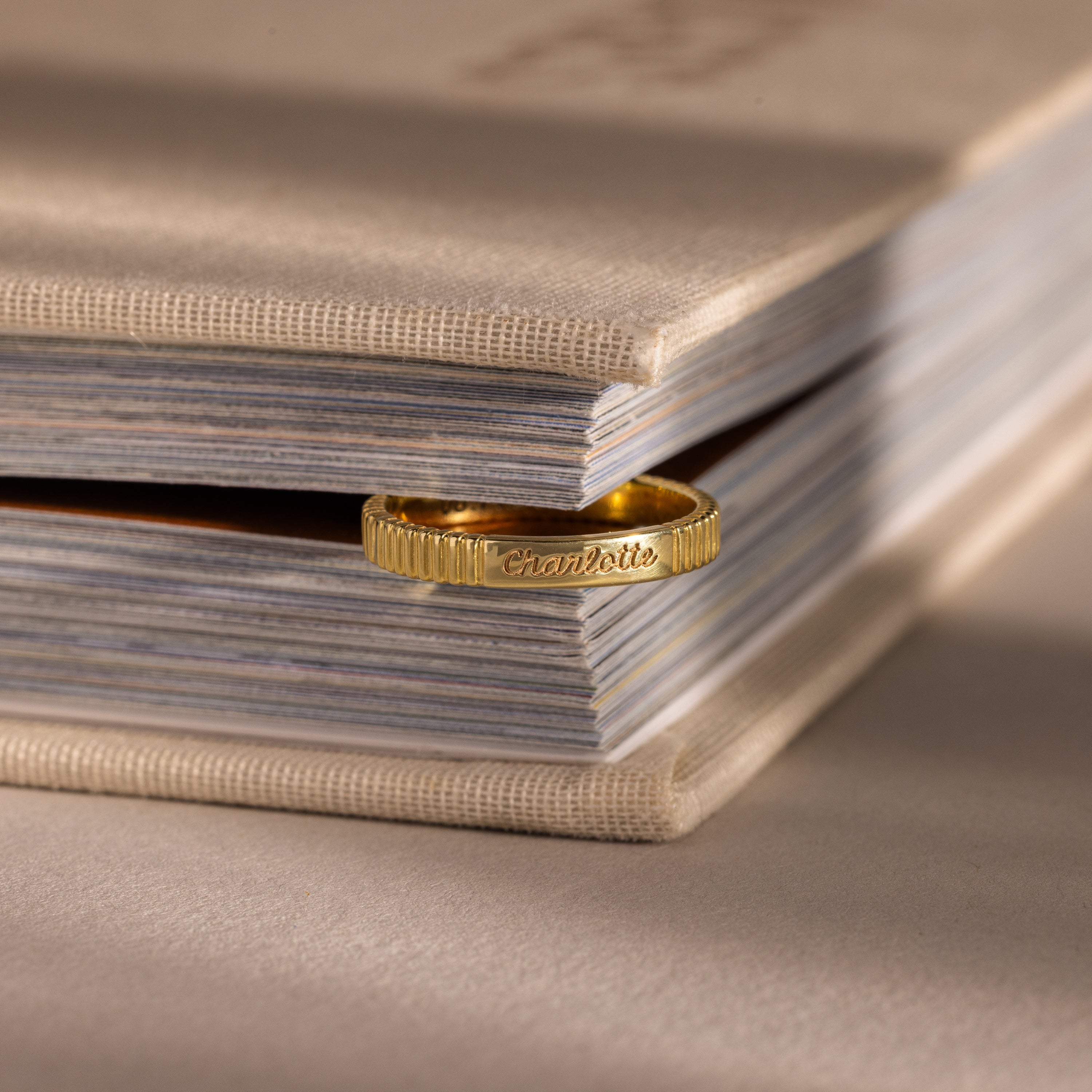 The Ribbed Name Ring in 18K Gold, engraved with "Charlotte," makes a unique bookmark inside a closed beige book.