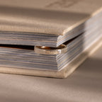 The Ribbed Name Ring in Silver, engraved with Mama, rests between the pages of a closed beige book—its personalized touch making this keepsake truly unique.