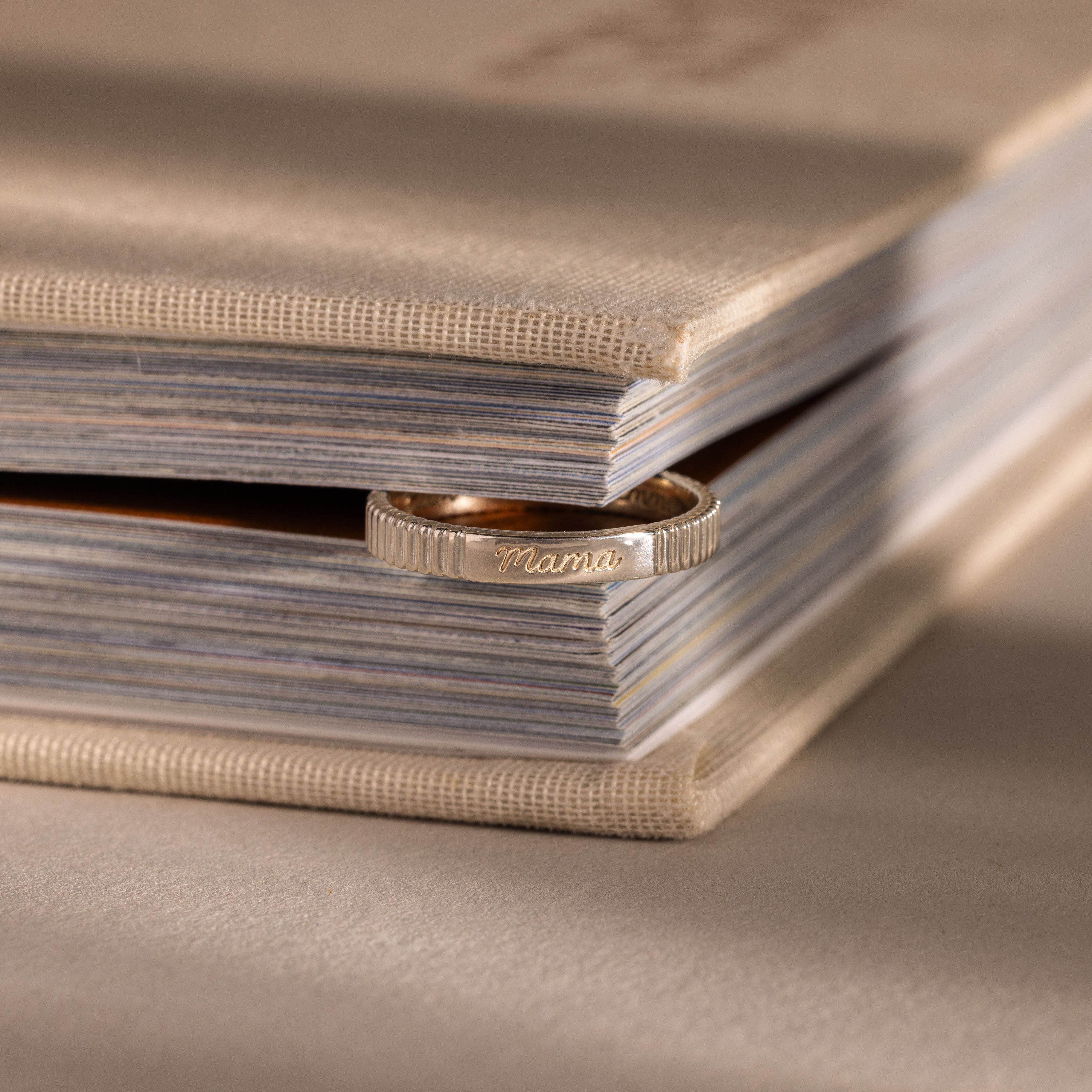 The Ribbed Name Ring in Silver, engraved with Mama, rests between the pages of a closed beige book—its personalized touch making this keepsake truly unique.
