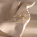 The Ribbed Name Signet Ring in Silver, engraved with the name Anna, rests on a softly curved beige surface.
