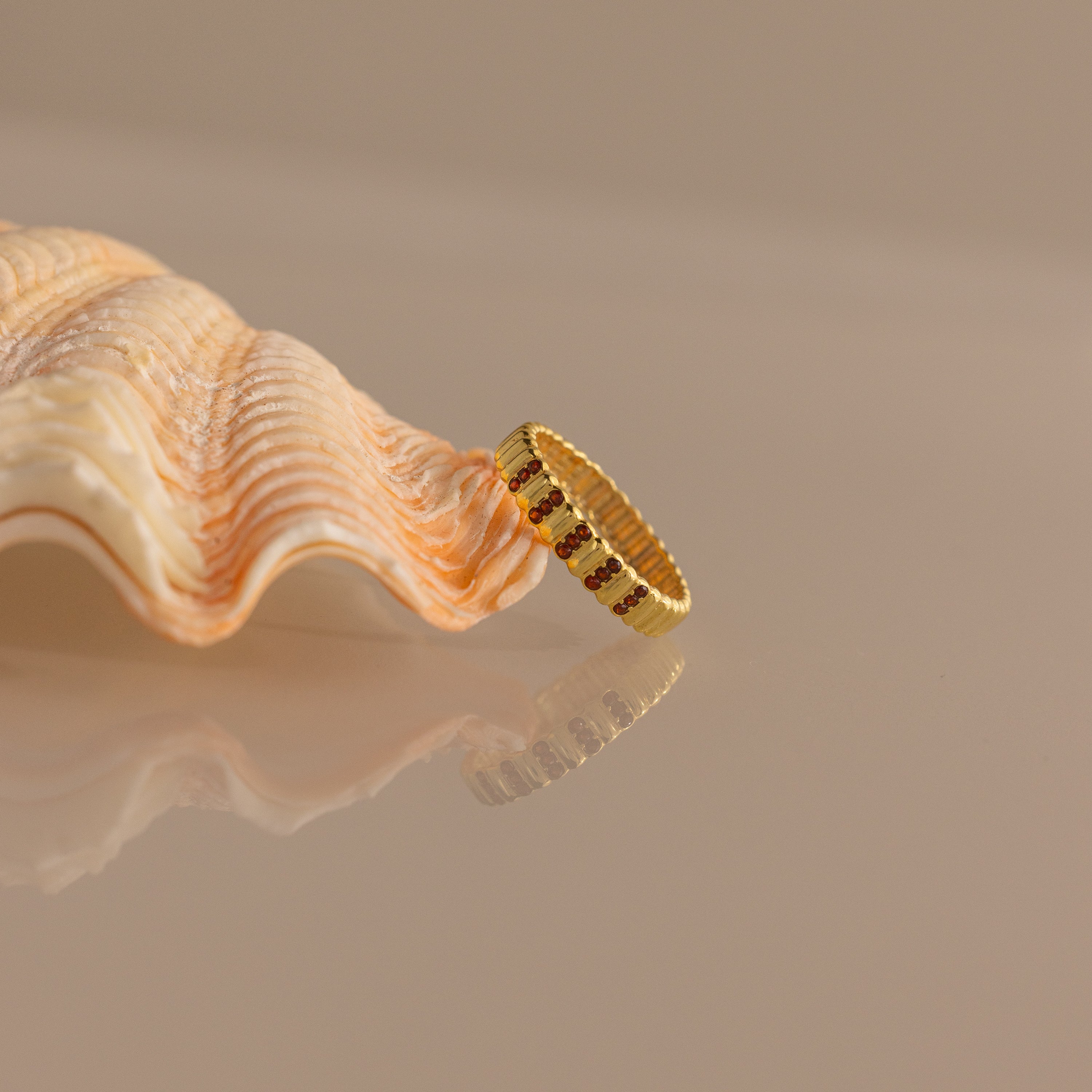 A Ribbed Triple Birthstone Ring is displayed against a light seashell on a reflective surface.