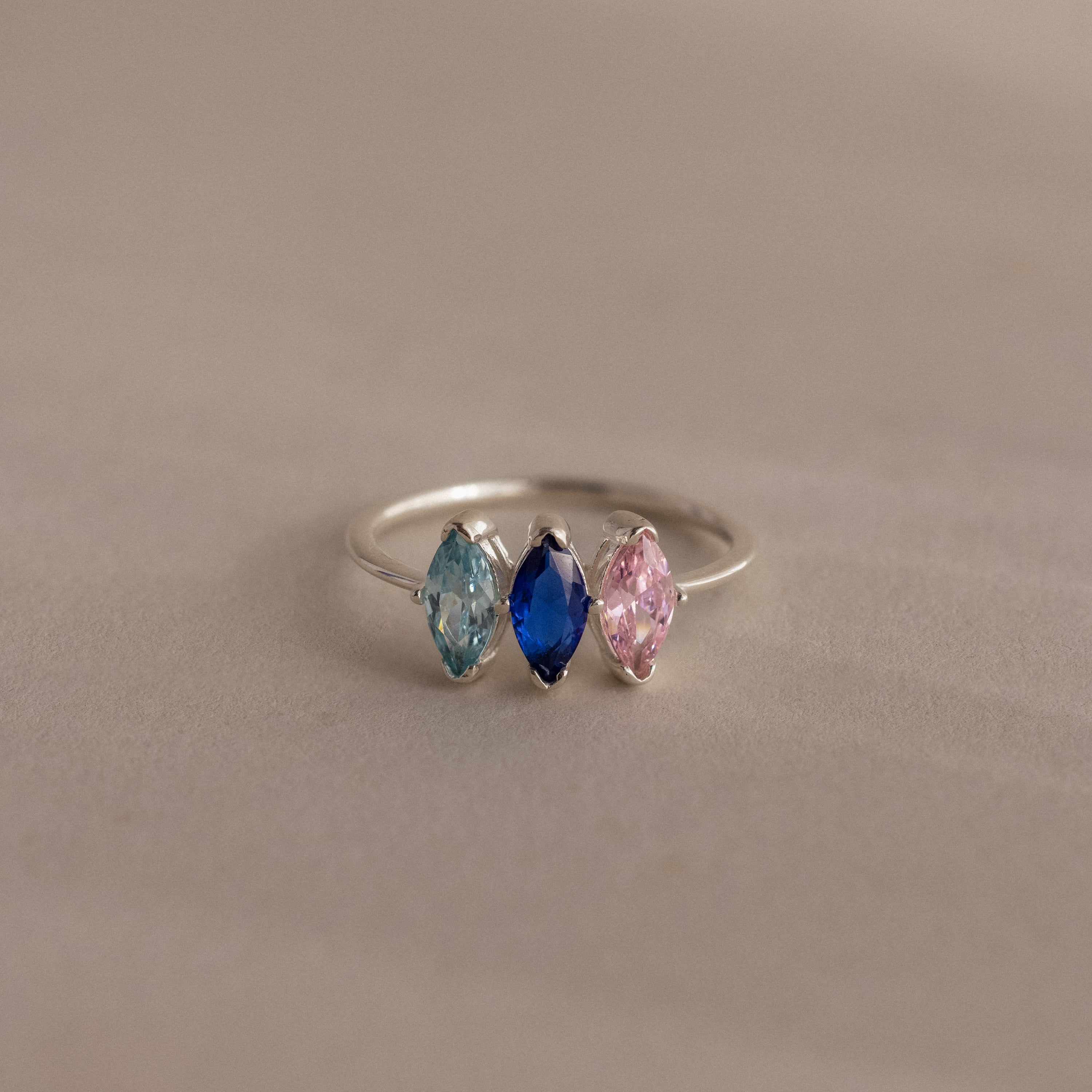 Celebrate special moments with the Multiple Marquise Birthstone Ring in Sterling Silver, featuring three marquise-cut stones—light blue, dark blue, and pink—side by side. A stunning personalized jewelry piece perfect for milestone gifts.