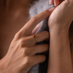 A hand with a rose gold Multiple Marquise Birthstone Ring featuring vibrant gemstones gently touches soft gray fabric—a beautiful, customizable piece of jewelry ideal for marking special milestones.