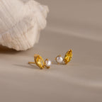 Marquise Topaz & Pearl Studs are displayed on a neutral surface near a white seashell.
