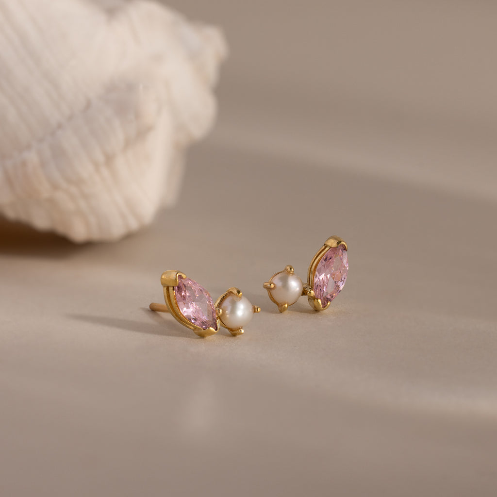 Marquise Pink Tourmaline & Pearl Studs displayed on a neutral surface near a seashell, featuring pink marquise stones and small pearls in a toi et moi design.