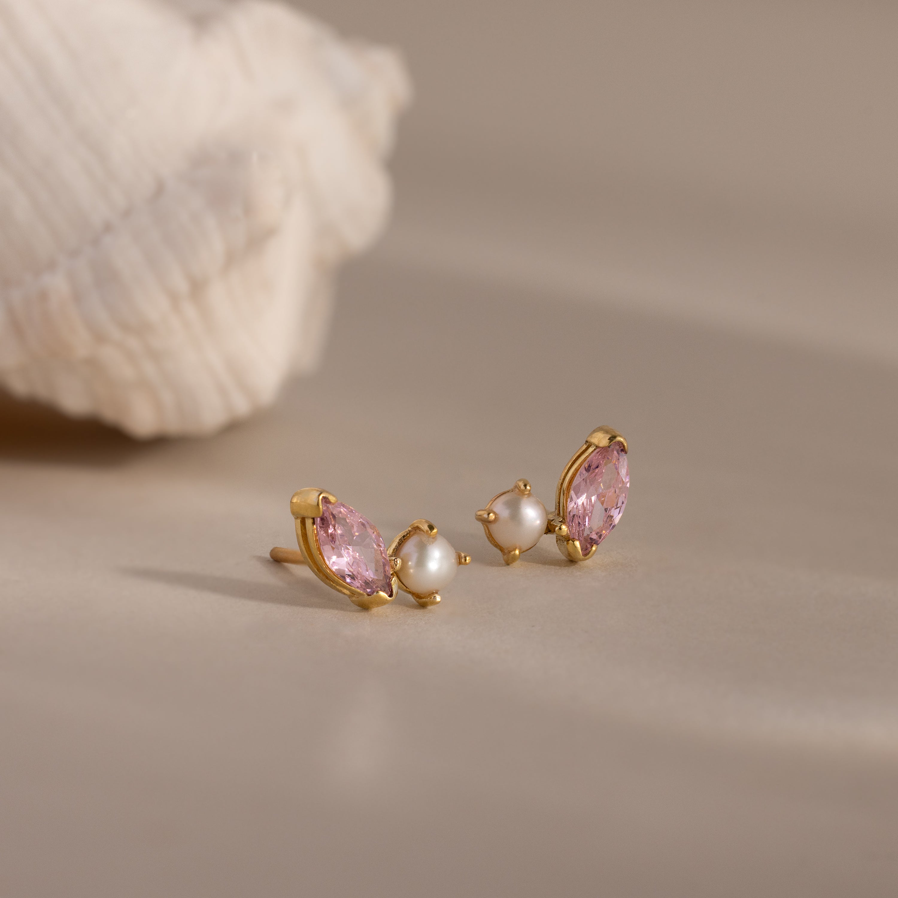 Marquise Pink Tourmaline & Pearl Studs displayed on a neutral surface near a seashell, featuring pink marquise stones and small pearls in a toi et moi design.