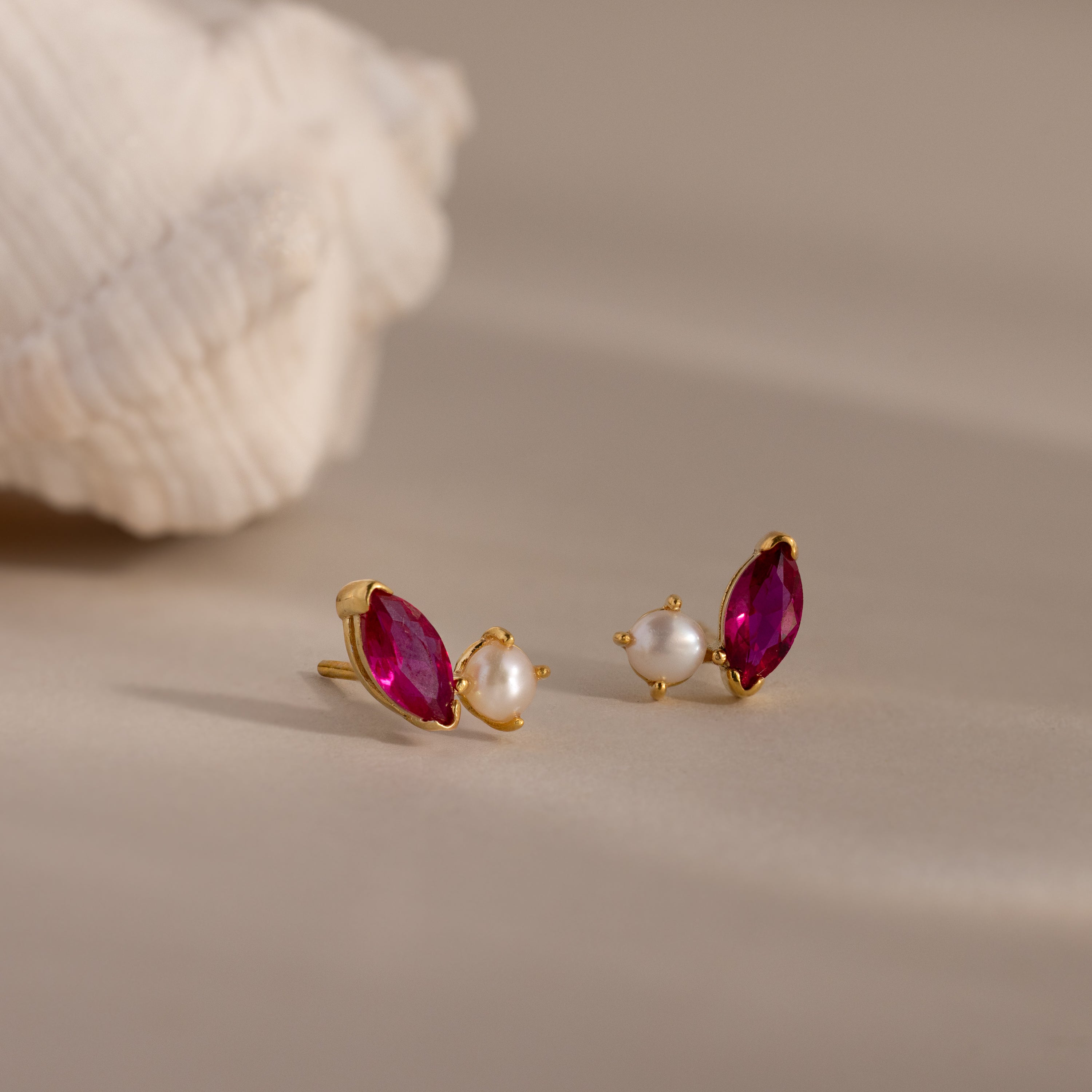 Marquise Ruby & Pearl Studs, featuring pink marquise stones and petite pearls, rest on a neutral surface near a seashell for a delicate update to classic pearl studs.