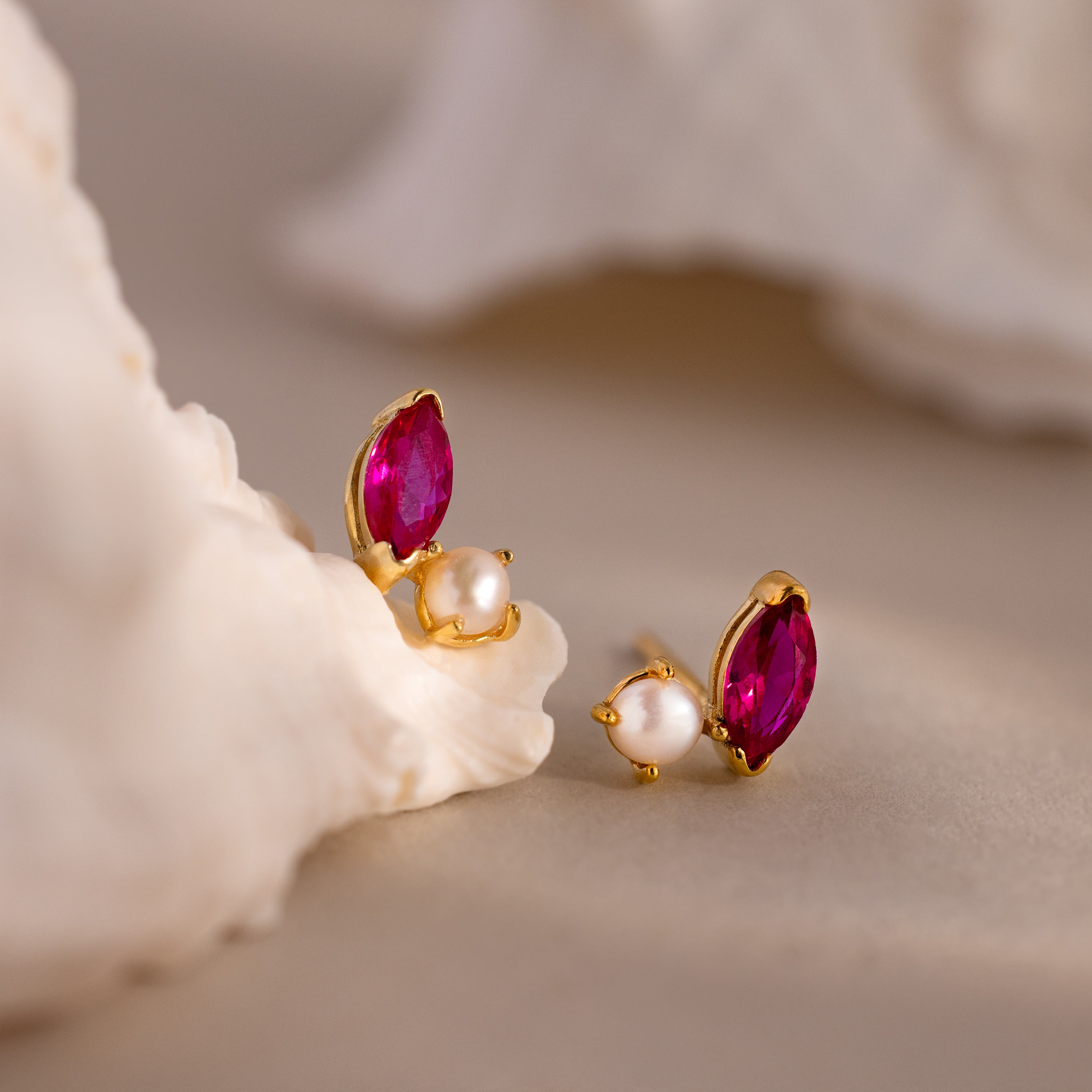 Marquise Birthstone & Pearl Studs feature gold settings with marquise pink stones and round pearls, displayed on a light, textured surface—a modern update to classic pearl earrings.