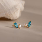 Marquise Blue Zircon & Pearl Studs—gold earrings featuring blue marquise zircon stones and small pearls, displayed on a neutral background with a shell.