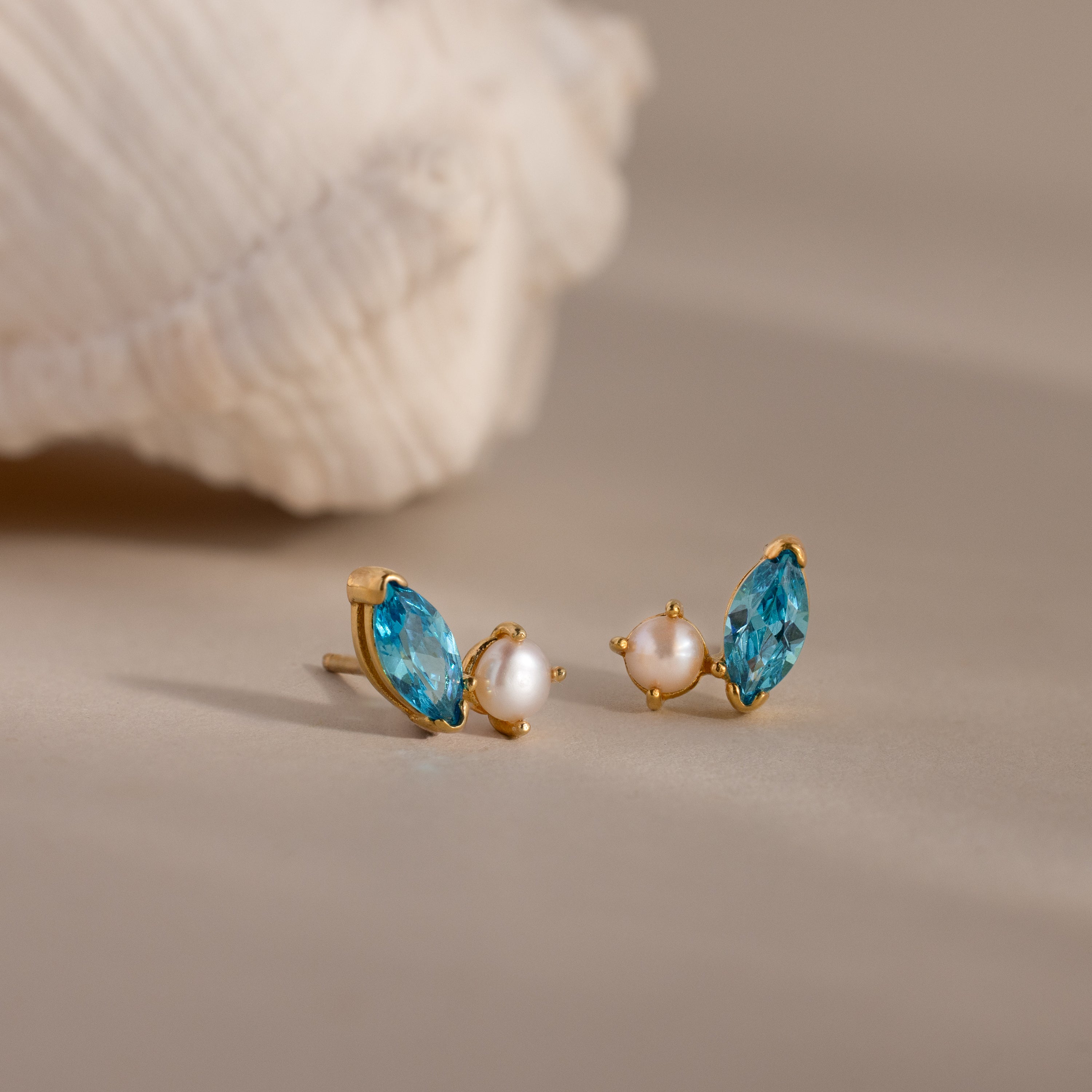 Marquise Blue Zircon & Pearl Studs—gold earrings featuring blue marquise zircon stones and small pearls, displayed on a neutral background with a shell.