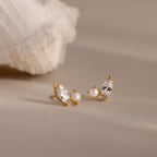 Marquise Opal & Pearl Studs—gold earrings featuring pearl and marquise opal details in a toi et moi design—are displayed on a neutral surface next to a seashell.