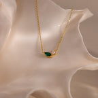 The Marquise Emerald & Pearl Necklace, featuring a green marquise birthstone and a small pearl, is displayed on a white seashell backdrop.