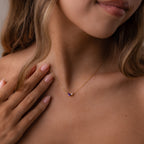 A woman with wavy hair touches her collarbone, wearing the Marquise Pink Tourmaline & Pearl Necklace featuring a delicate, customizable pendant.