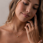 A woman smiles softly, touching her face as she wears the Marquise Onyx & Pearl Necklace, featuring lustrous pearls.