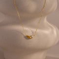 The Marquise Topaz & Pearl Necklace features a gold chain with a small leaf charm and pearl pendant, displayed on a textured light surface. This elegant necklace can be customized as a unique birthstone piece for a personal touch.