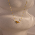 The Marquise Topaz & Pearl Necklace features a gold chain with a small leaf charm and pearl pendant, displayed on a textured light surface. This elegant necklace can be customized as a unique birthstone piece for a personal touch.