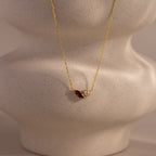 The Marquise Garnet & Pearl Necklace features a marquise-shaped garnet birthstone and a small pearl pendant, elegantly displayed on a textured beige bust.