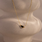 Marquise Onyx & Pearl Necklace featuring a gold chain with a black marquise onyx and small white freshwater pearl pendant, shown on a textured beige display.
