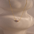 The Marquise Alexandrite & Pearl Necklace features a marquise-cut purple alexandrite and a pearl, displayed on a textured, wavy cream-colored stand.