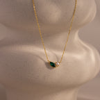 The Marquise Emerald & Pearl Necklace features a green marquise emerald birthstone and a delicate pearl pendant, displayed on a textured, sculpted surface.