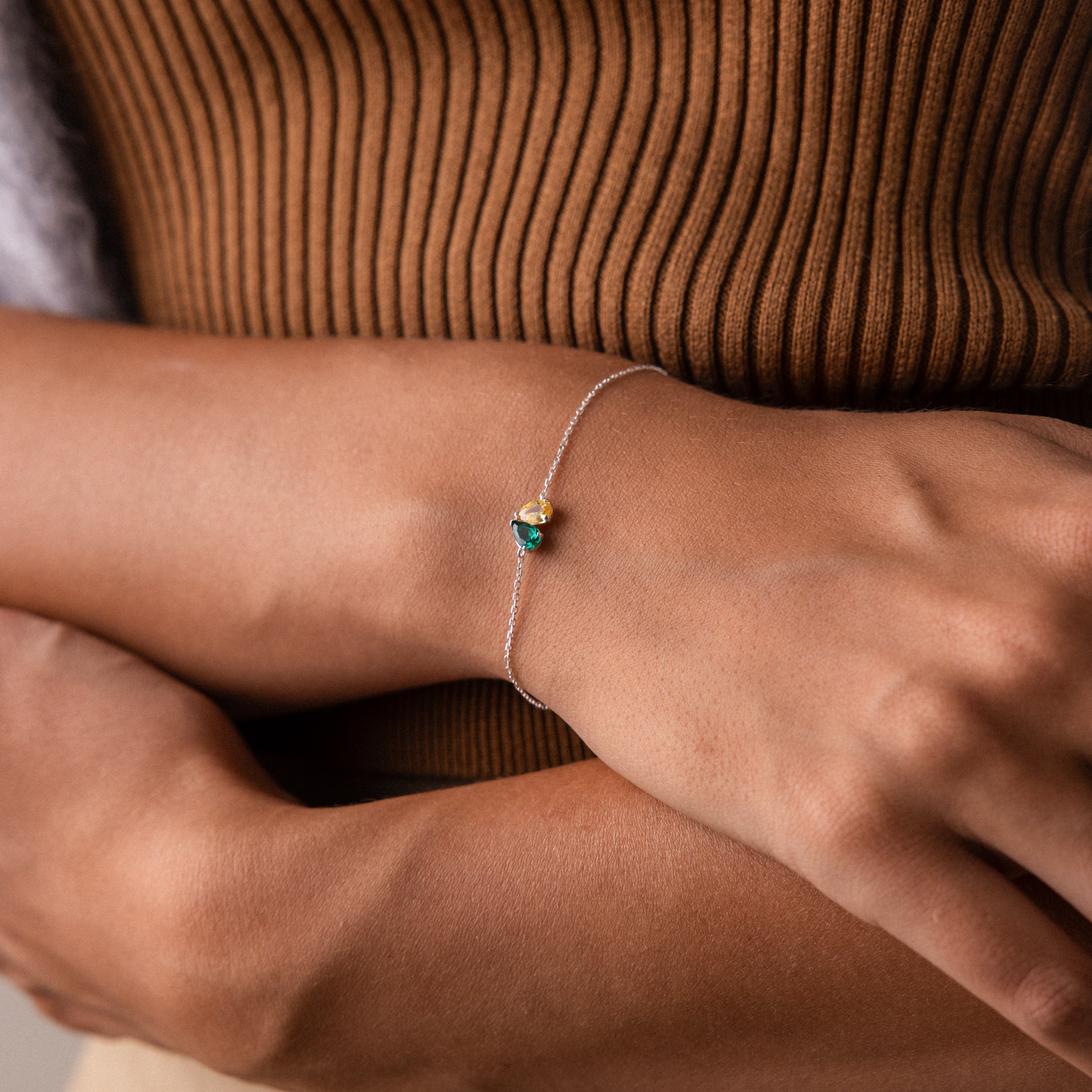 The Toi et Moi Teardrop Heart Bracelet, featuring a delicate silver teardrop heart and a small blue and gold charm, adorns a person’s wrist.