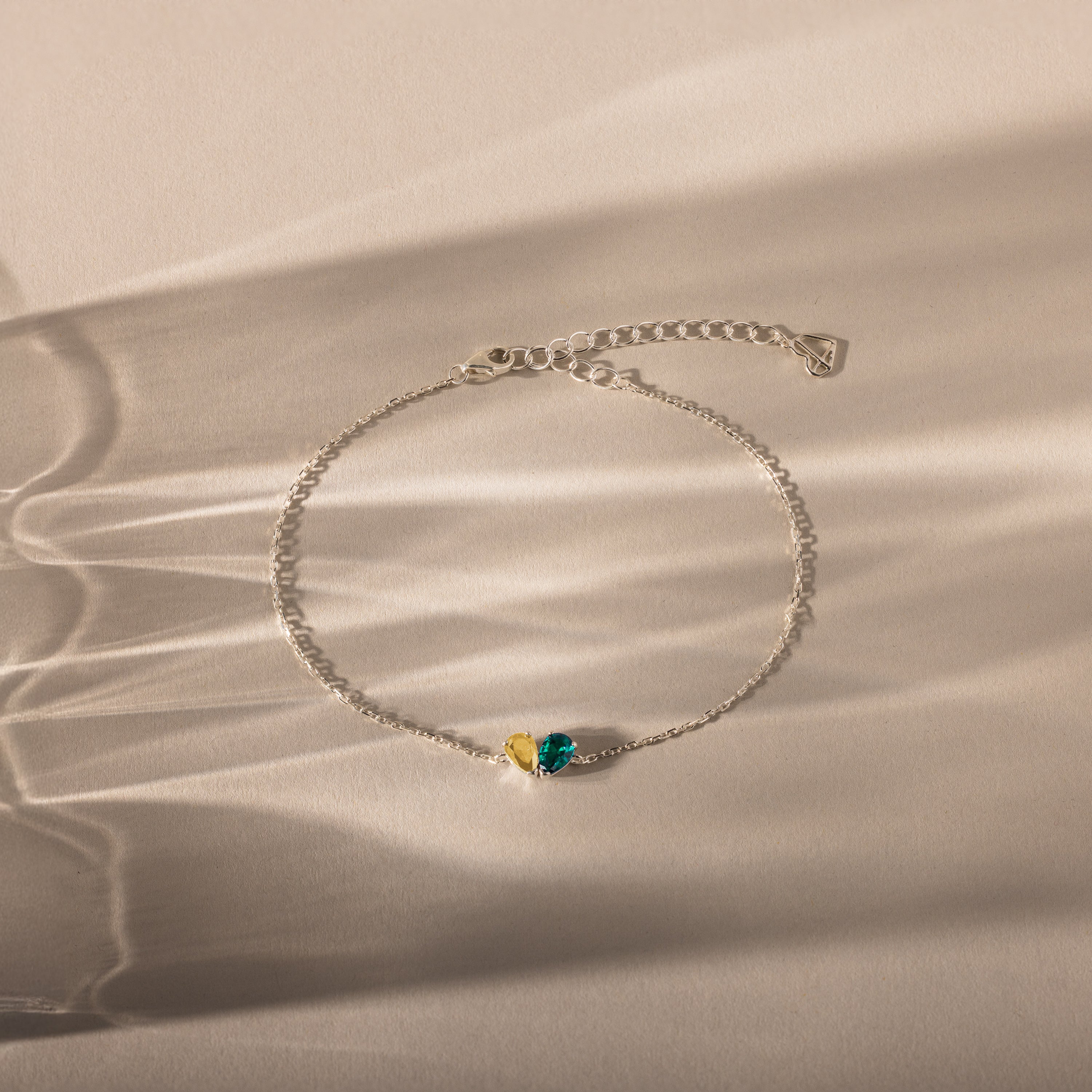 The Toi et Moi Teardrop Heart Bracelet in Sterling Silver features yellow and green gemstones, displayed on a neutral background with soft shadows.