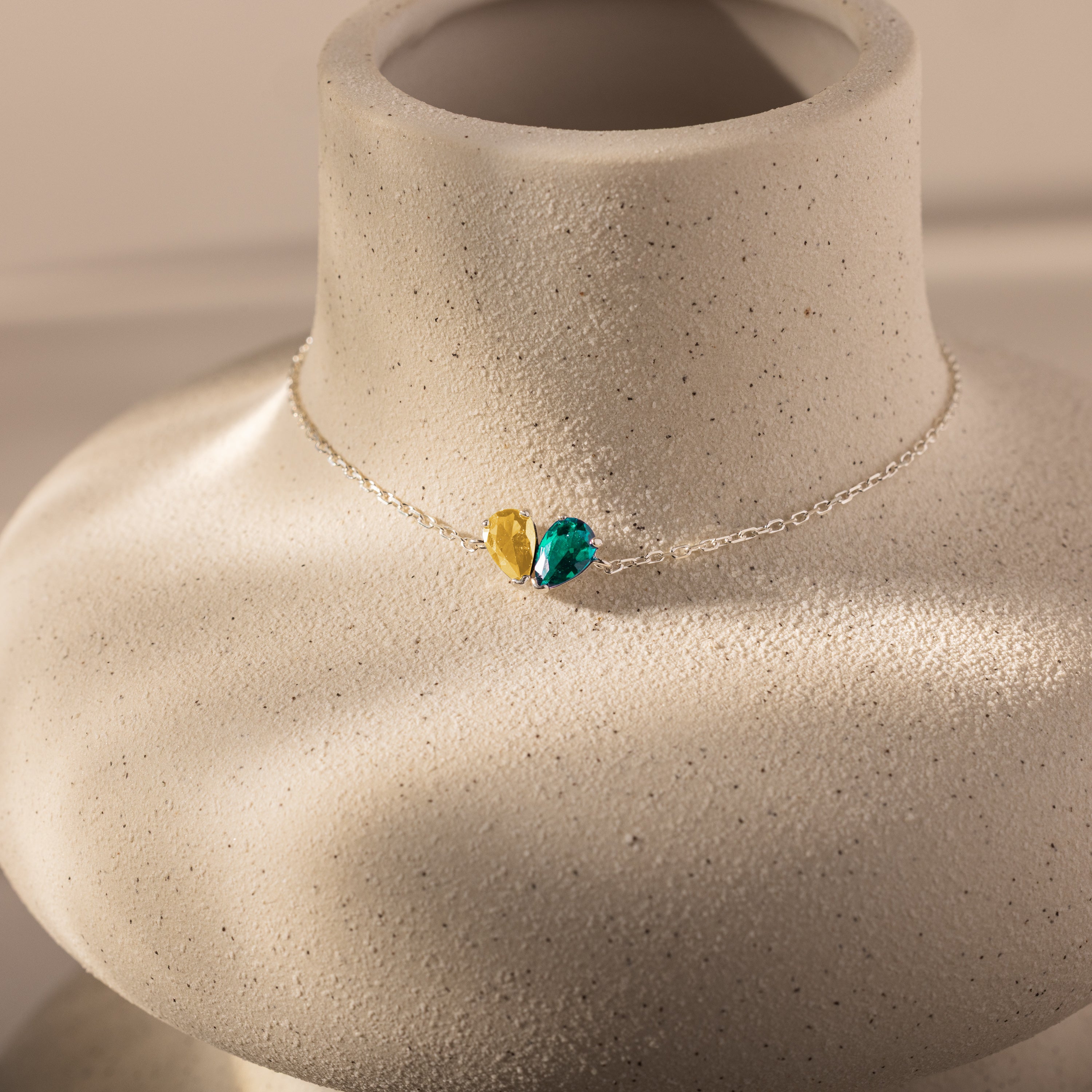 Elegant Toi et Moi Teardrop Heart Bracelet in sterling silver, featuring yellow and teal pear-cut stones, beautifully presented on a textured stone bust.