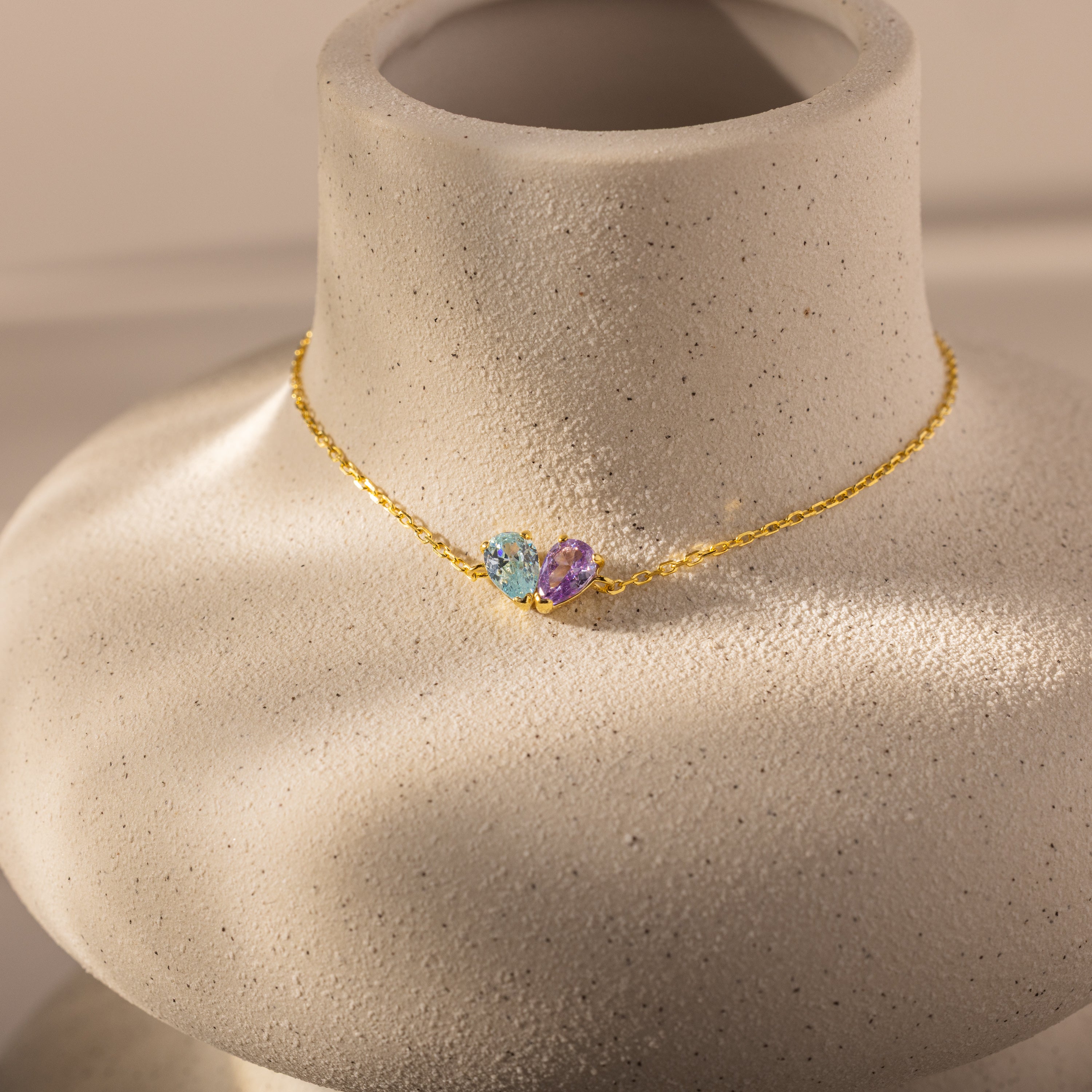 The Toi et Moi Teardrop Heart Bracelet in 18K Gold features two heart-shaped gemstones, one blue and one purple pear cut, elegantly showcased.