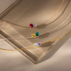 The Toi et Moi Teardrop Heart Bracelet, featuring a colorful gemstone heart pendant that shimmers like a pear-cut stone, rests elegantly on a frosted glass surface.